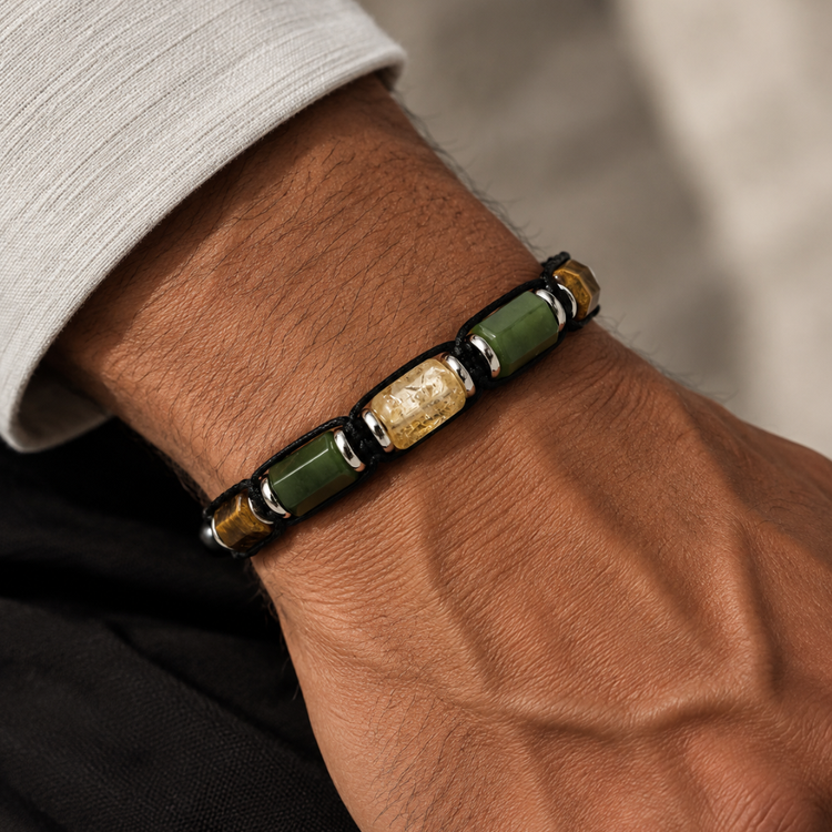 A close-up of a beaded bracelet worn on a person's wrist. The bracelet features alternating green stone beads and metallic gold-toned beads separated by small silver spacer rings, set against a dark background with a light gray sleeve visible.